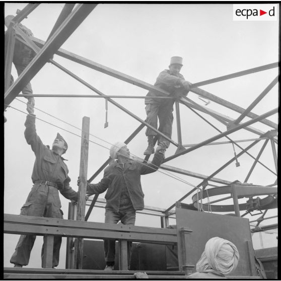 Deux soldats et un jeune algérien travaillant sur le toit d'un hangar en chantier.