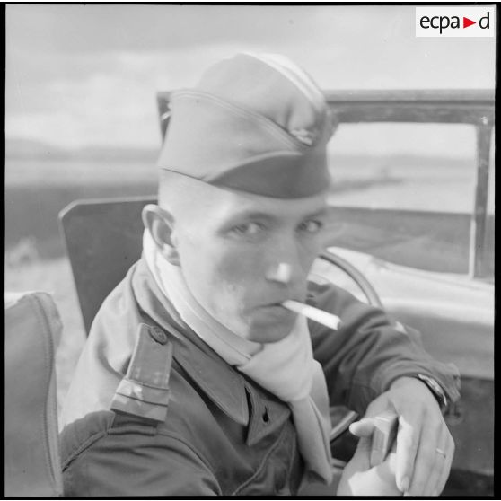 Portrait d'un lieutenant fumant une cigarette à bord d'un véhicule léger militaire en Algérie.
