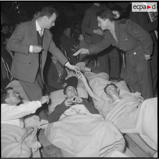 Le comédien Fernand Raynaud distribue des autographes aux blessés de l'hôpital militaire Maillot à Alger.