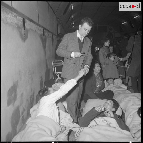 Le comédien Fernand Raynaud distribue des autographes aux blessés de l'hôpital militaire Maillot à Alger.