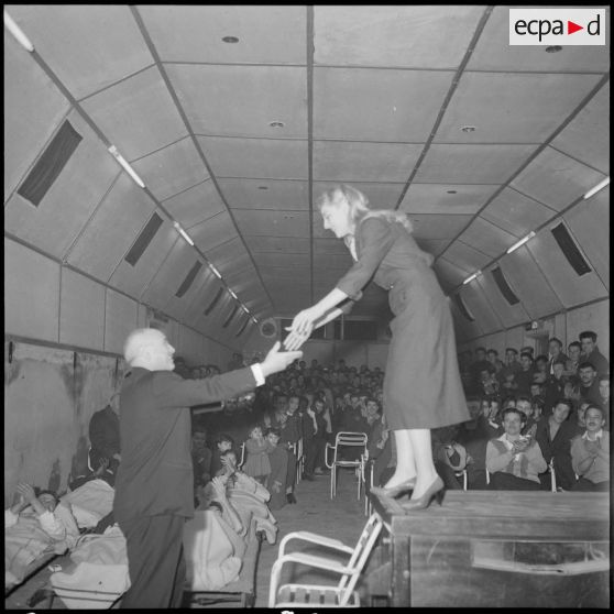 Jean Nohain aide la chanteuse Danièle Dupré à descendre de scène lors d'une représentation à l'hôpital Maillot d'Alger.