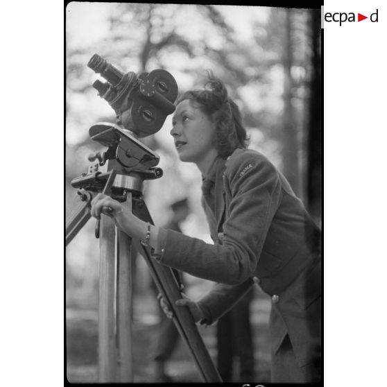 Une volontaire féminine de la France libre filme à l'aide d'une caméra Bell et Howell sur trépied.