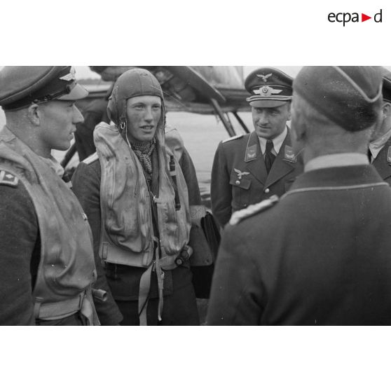 Un pilote d'hydravion Arado Ar-95 descend de son appareil, une mallette à la main, des officiers de la Luftwaffe l'attendent.