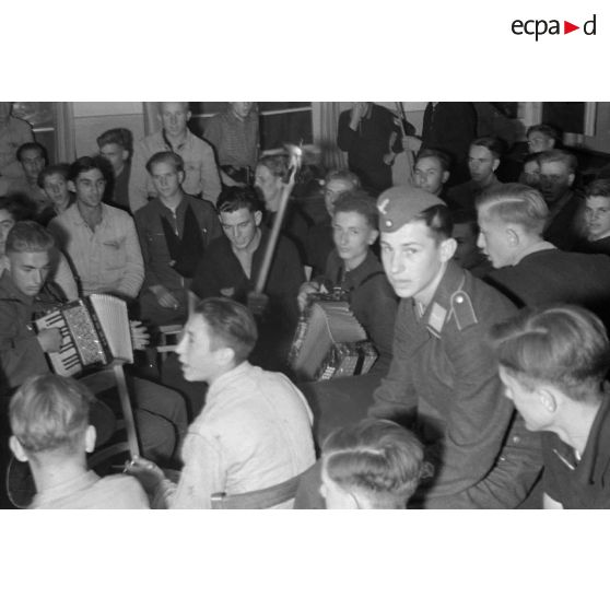 Des jeunes membres du N.S.F.K. chantent et jouent de la musique. Au milieu d'eux, une jeune recrue de la Luftwaffe.