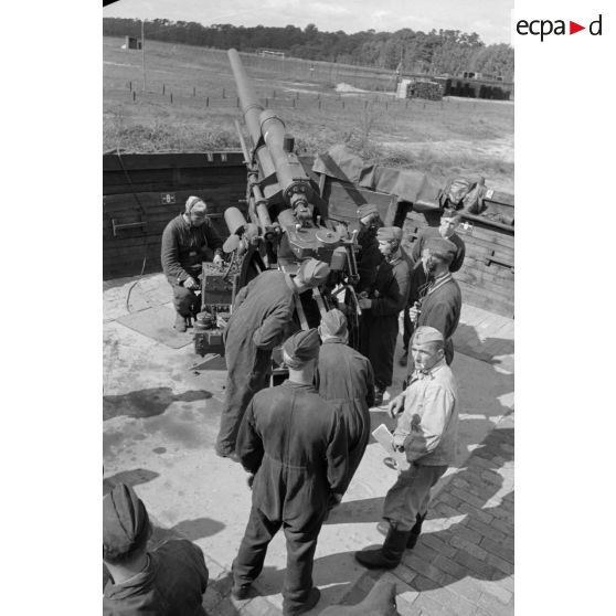 Mise en batterie d'une pièce de 8,8-cm-FlaK-18-L56, placée dans un abri en bois.