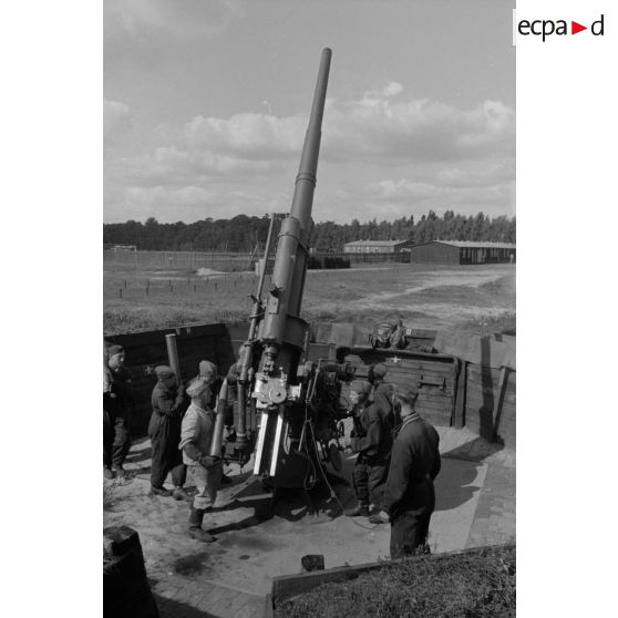 Mise en batterie d'une pièce de 8,8-cm-FlaK-18-L56, placée dans un abri en bois.