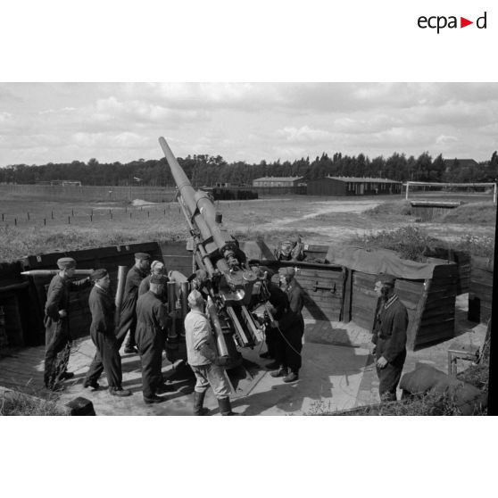 Mise en batterie d'une pièce de 8,8-cm-FlaK-18-L56, placée dans un abri en bois.
