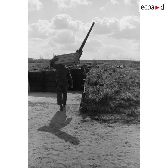 Des servants d'une pièce de Flak calibre 8,8 cm Flak 18-L56, dans un poste en bois, apportent des caissons de munitions, sur leur dos.