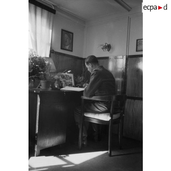 Un officier de la DCA de l'armée de l'air allemande (FlaK) ecrit une lettre, assis derrière son bureau.