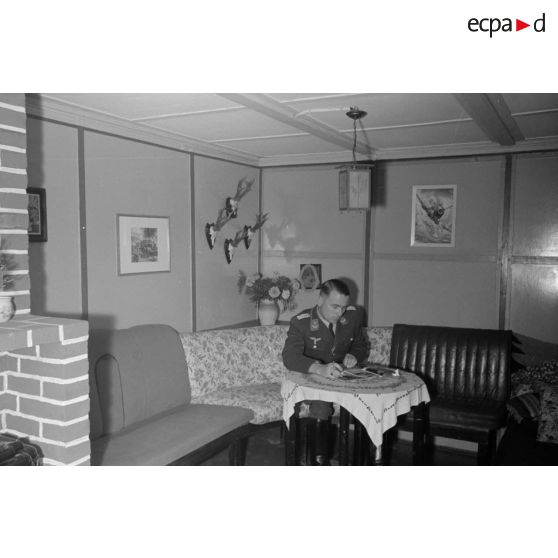 Dans ses quartiers, un lieutenant (Oberleutnant) de la DCA de l'armée de l'air allemande (FlaK) lit des magazines en fumant le cigare.