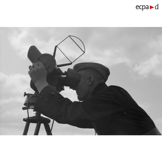 Un observateur de la FlaK, scrute le ciel dans un binoculaire monté sur trépied.
