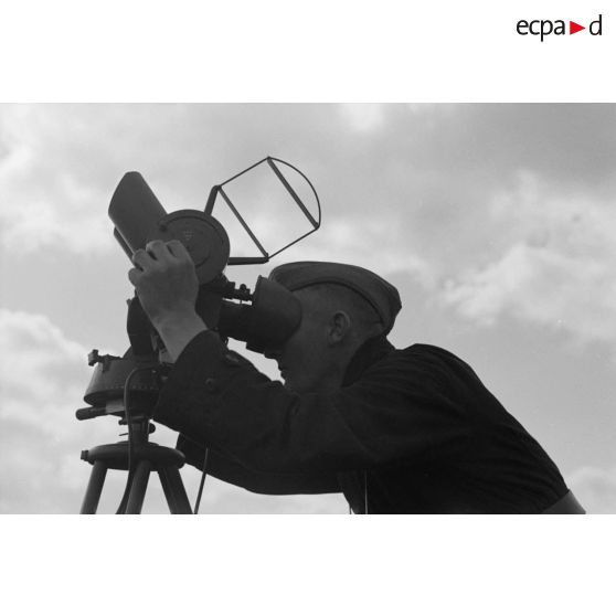 Un observateur de la FlaK, scrute le ciel dans un binoculaire monté sur trépied.