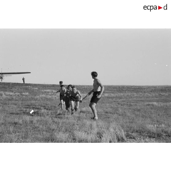 Des jeunes du Nationalsozialistischen Flieger-Korps (N.S.F.K.) courent, en tirant sur une corde, destinée à donner sa vitesse de décollage à un planeur léger.