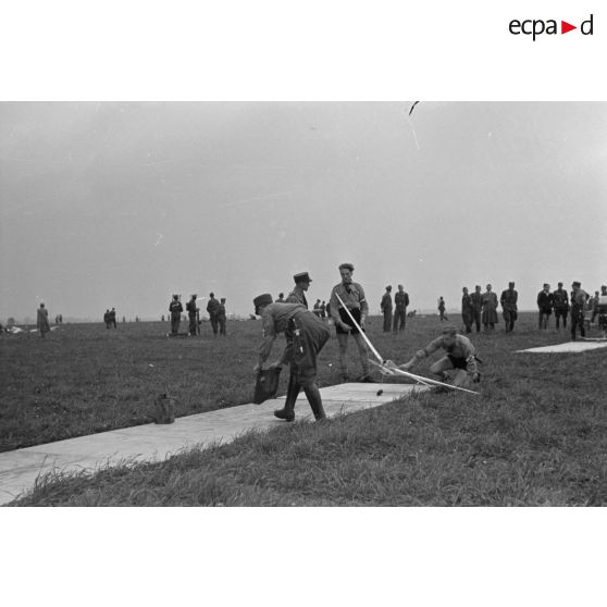 Deux membres des Hitlerjugend installent un modéle réduit d'avion sur son aire de décollage, sous la surveillance d'un Truppführer du N.S.F.K.