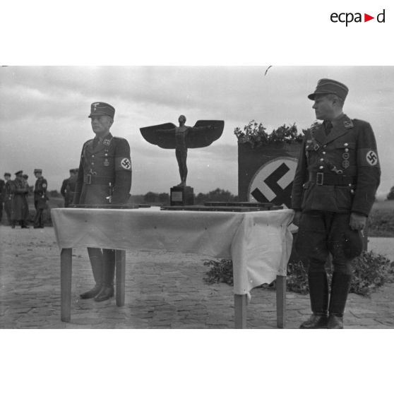 Deux officiers du N.S.F.K. : un Sturmbannführer et un Hauptsturmführer, encadrent une table où sont posés des trophées du N.S.F.K.