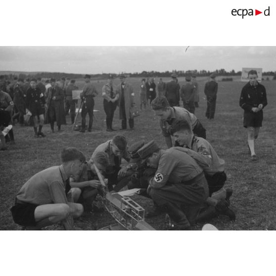 Des membres de la Hitlerjugend et des membres du N.S.F.K s'affairent autour d'un modèle réduit d'avion partiellement détoilé.