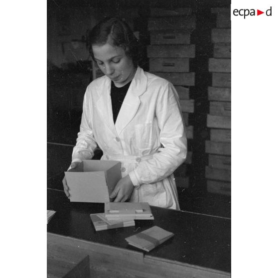 Une femme en blouse blanche prépare un carton d'emballage.