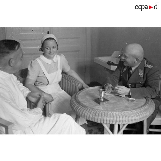 Un médecin et une infirmière discutent avec un capitaine (Hauptmann) de la Luftwaffe, peut-être un membre d'une compagnie de propagande.