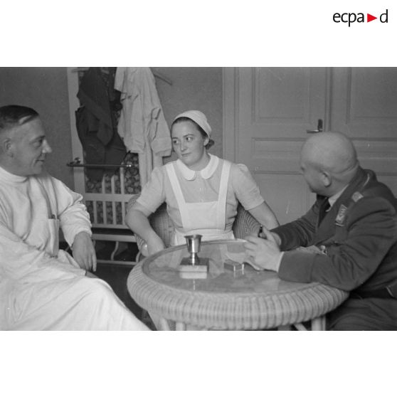 Un médecin et une infirmière discutent avec un capitaine (Hauptmann) de la Luftwaffe, peut-être un membre d'une compagnie de propagande.