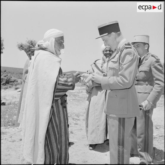 El Gor, Algérie. Un capitaine de la 1re compagnie du 21e régiment d'infanterie (RI) distribue des cigarettes à la population.