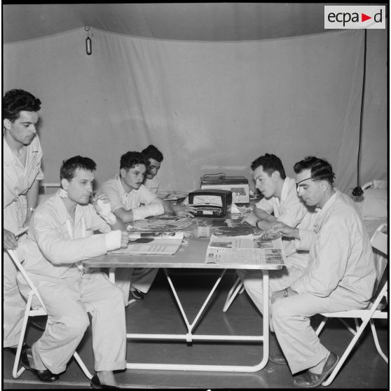 Centre médical de Maison-Blanche. Patients attablés et lisant sous la tente.