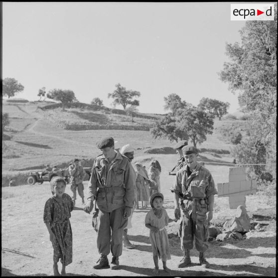 Au douar de Beni Chimerane, des parachutistes tiennent des enfants du village par la main.