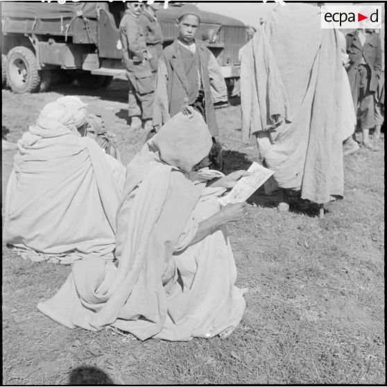 Les habitants du douar s'interessent aux tracts que leur distribuent les soldats.