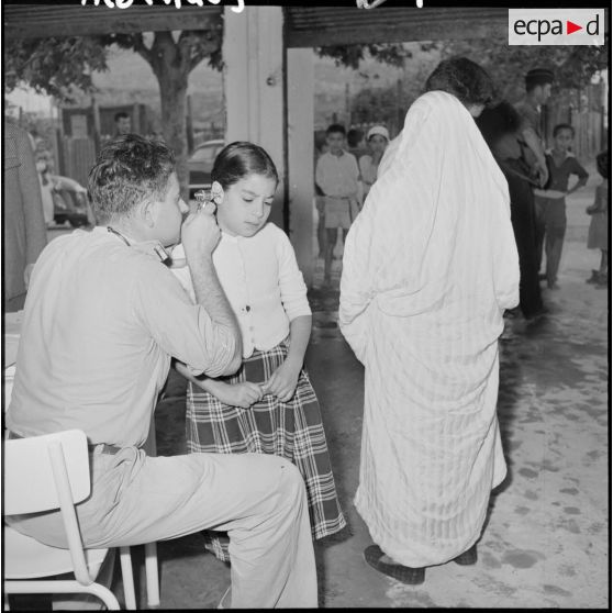 Le sous-lieutenant médecin, détaché de l'école militaire, ausculte les enfants malades.