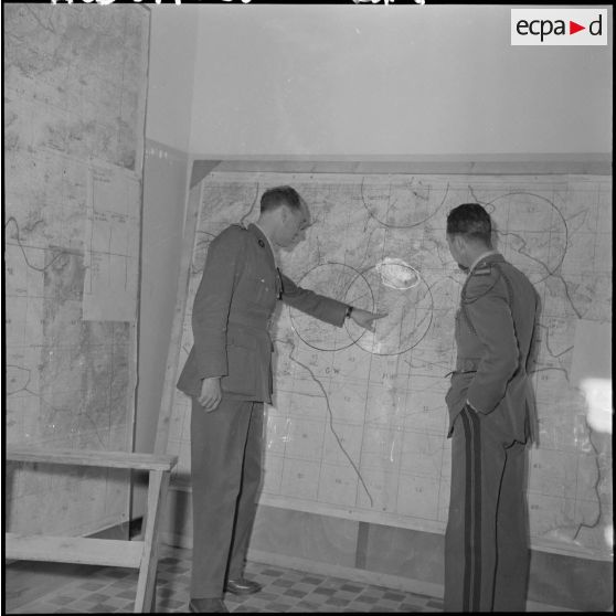 Deux autorités militaires discutant de stratégie devant une carte dans leur bureau.