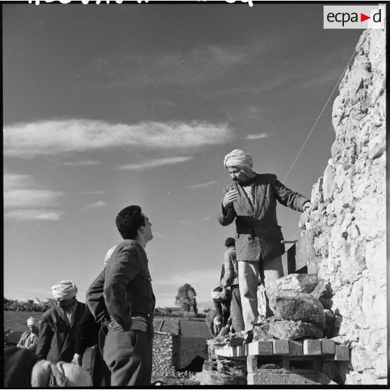 Sur le chantier de l'école de Ouled Mohamed l'officier d'action psychologique demande les besoins en matériaux aux maçons du Douar.