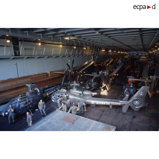 Dans un hangar du TCD (transport de chalands de débarquement) Foudre s'alignent des hélicoptères de combat Gazelle de l'ALAT (aviation légère de l'armée de terre), pales repliées ou démontées du rotor.