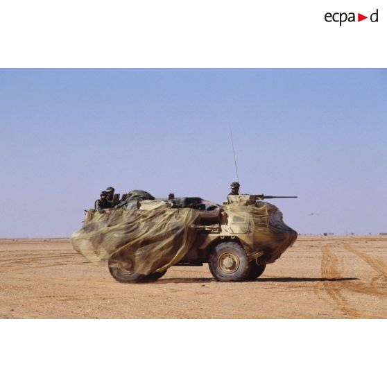 VAB à l'arrêt en zone Miramar, recouvert d'un filet de camouflage. Le chef de tir est à son poste, derrière sa mitrailleuse.