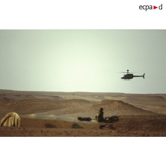 En ZDO (zone de déploiement opérationnel) Olive, un hélicoptère américain de reconnaissance et d'observation Bell-OH58 Kiowa muni d'un système de visée pour la lutte antichar monté sur mat au-dessus du rotor survole un camion du 1er RS (régiment de spahis) posté dans le désert.