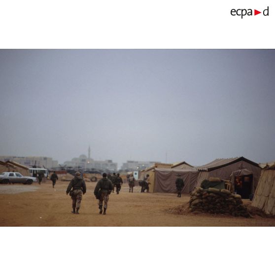 Le camp américain et la mosquée de CRK (camp du roi Khaled) au loin. Des soldats vus de dos parcourent l'avenue principale.