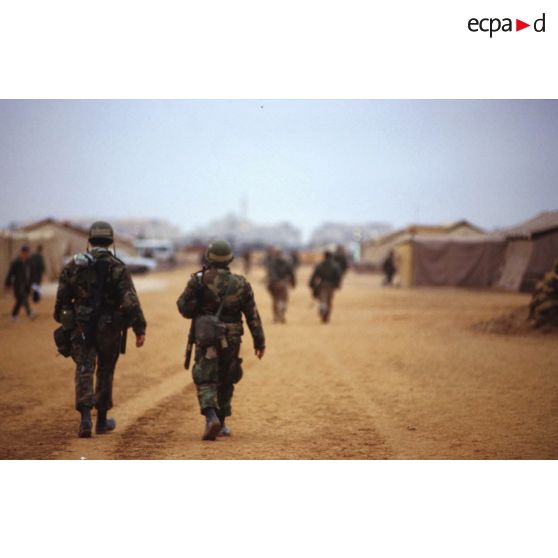 Le camp américain et la mosquée de CRK (camp du roi Khaled) au loin. Des soldats vus de dos parcourent l'avenue principale.