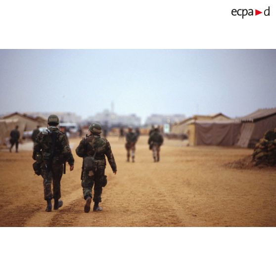 Le camp américain et la mosquée de CRK (camp du roi Khaled) au loin. Des soldats vus de dos parcourent l'avenue principale.