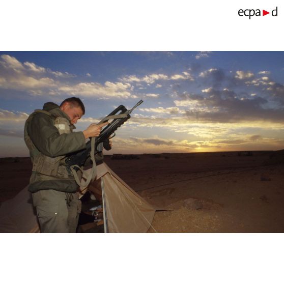 En ZDO (zone de déploiement opérationnel) Olive, sentinelle armée d'un fusil d'assaut FAMAS devant sa tente au coucher de soleil.