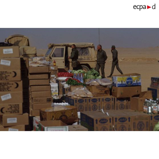 Au centre d'approvisionnement au CRK (camp du roi Khaled), les caisses de rations de combat et cartons de vivres sont entassés en extérieur. A l'arrière-plan, un véhicule Peugeot P4.