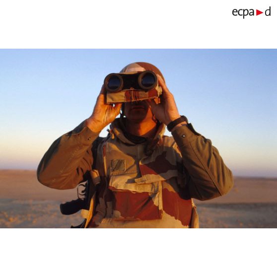 En ZDO (zone de déploiement opérationnel) Olive, un soldat est posté en observation dans le désert, équipé de jumelles.