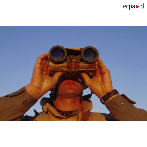 En ZDO (zone de déploiement opérationnel) Olive, un soldat est posté en observation dans le désert, équipé de jumelles.