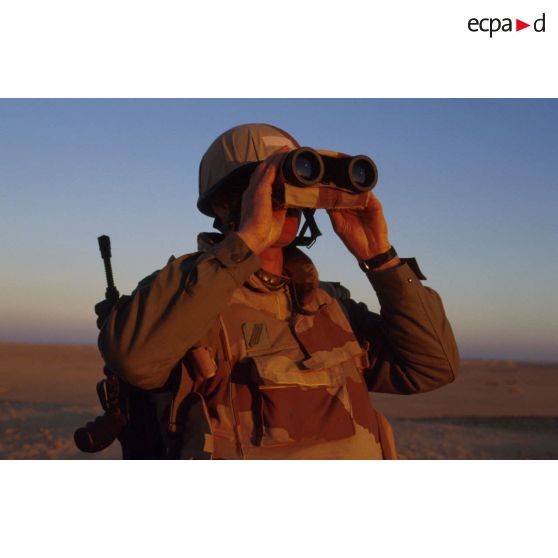 En ZDO (zone de déploiement opérationnel) Olive, un soldat est posté en observation dans le désert, équipé de jumelles.