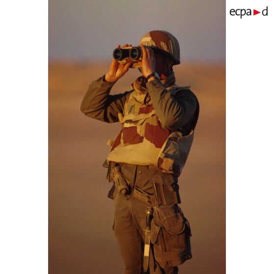 En ZDO (zone de déploiement opérationnel) Olive, un soldat est posté en observation dans le désert, équipé de jumelles.