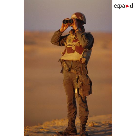 En ZDO (zone de déploiement opérationnel) Olive, un soldat est posté en observation dans le désert, équipé de jumelles.