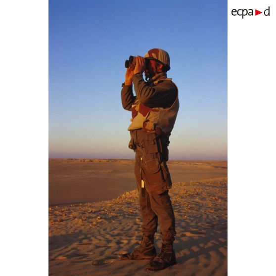 En ZDO (zone de déploiement opérationnel) Olive, un soldat est posté en observation dans le désert, équipé de jumelles.