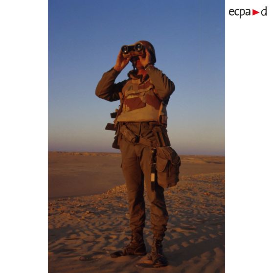 En ZDO (zone de déploiement opérationnel) Olive, un soldat est posté en observation dans le désert, équipé de jumelles.