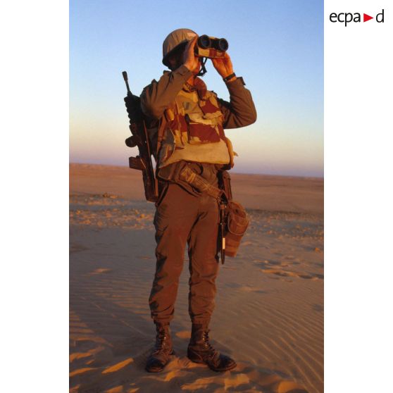 En ZDO (zone de déploiement opérationnel) Olive, un soldat est posté en observation dans le désert, équipé de jumelles.