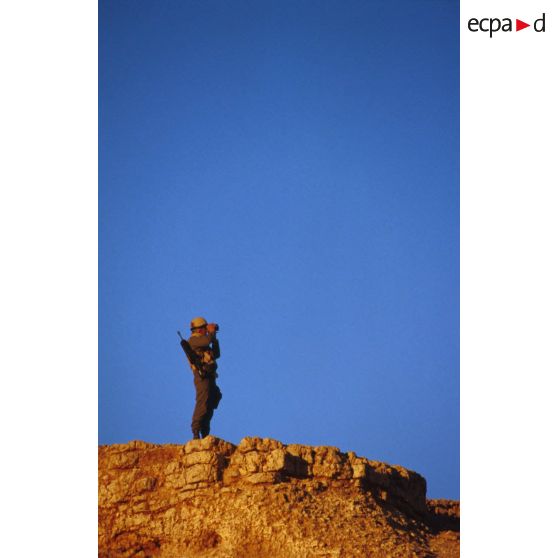 En ZDO (zone de déploiement opérationnel) Olive, un soldat équipé de jumelles est posté en observation au sommet d'une butte.