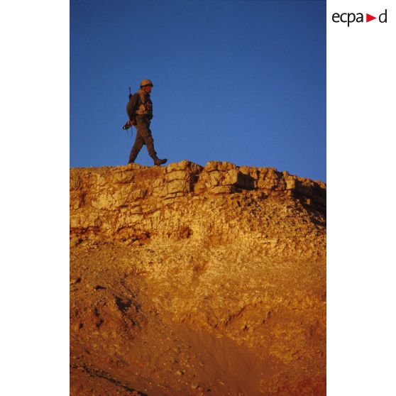 En ZDO (zone de déploiement opérationnel) Olive, un soldat équipé de jumelles est posté en observation au sommet d'une butte.
