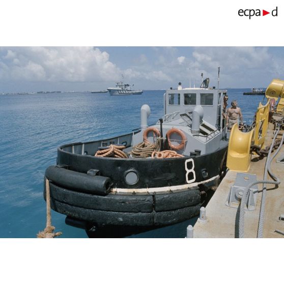 La barge de mise en place des containers est déplacée par les remorqueurs de la Marine dans le port de Mururoa. [Description en cours]