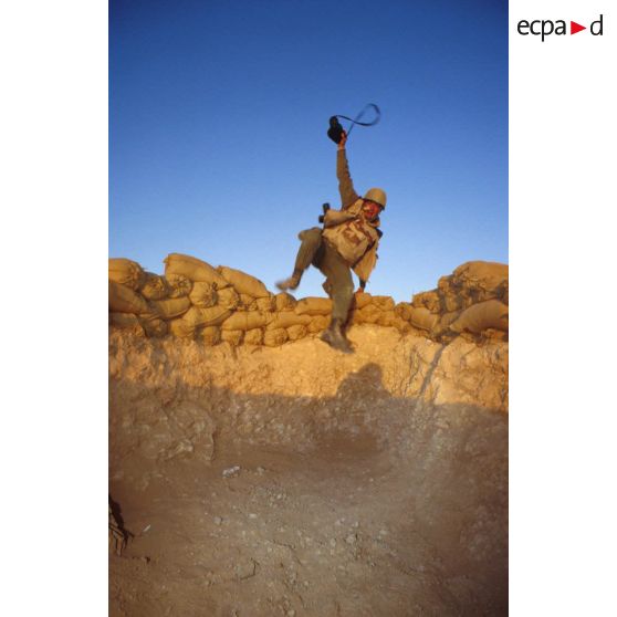 En ZDO (zone de déploiement opérationnel) Olive, un sergent photographe de l'ECPA (Etablissement cinématographique et photographique des Armées) saute par-dessus le muret de sacs de sable dans son trou de combat.